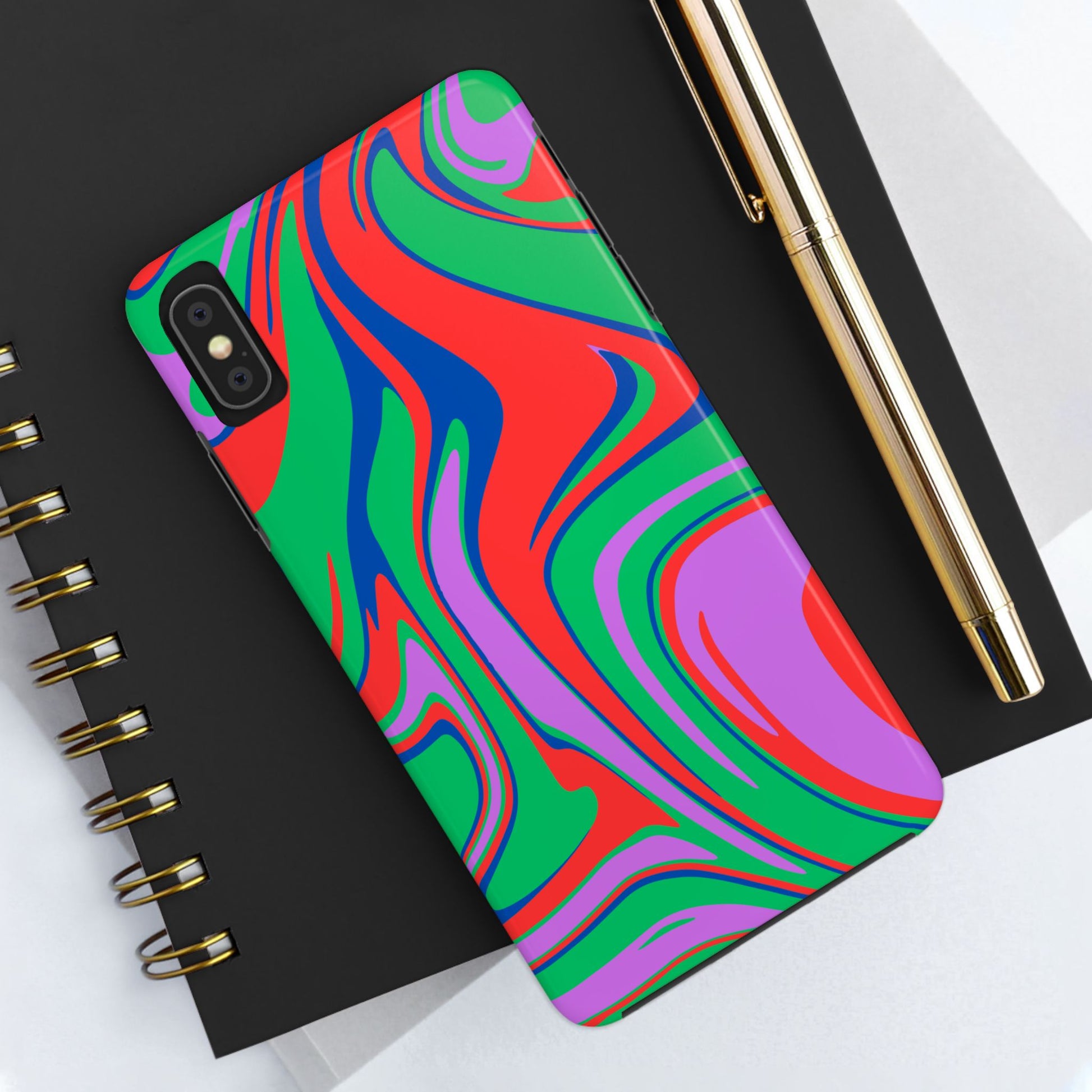 A Colorful Zebra Print Phone Case with a bold red, green, blue, and purple design sits on a black spiral notebook next to a gold pen on a white surface.