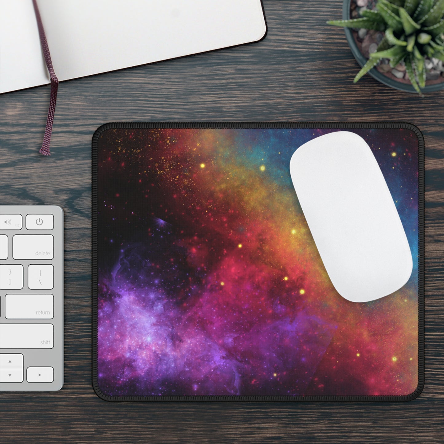 Colorful galaxy gaming mouse pad on a wooden desk with keyboard and notebook
