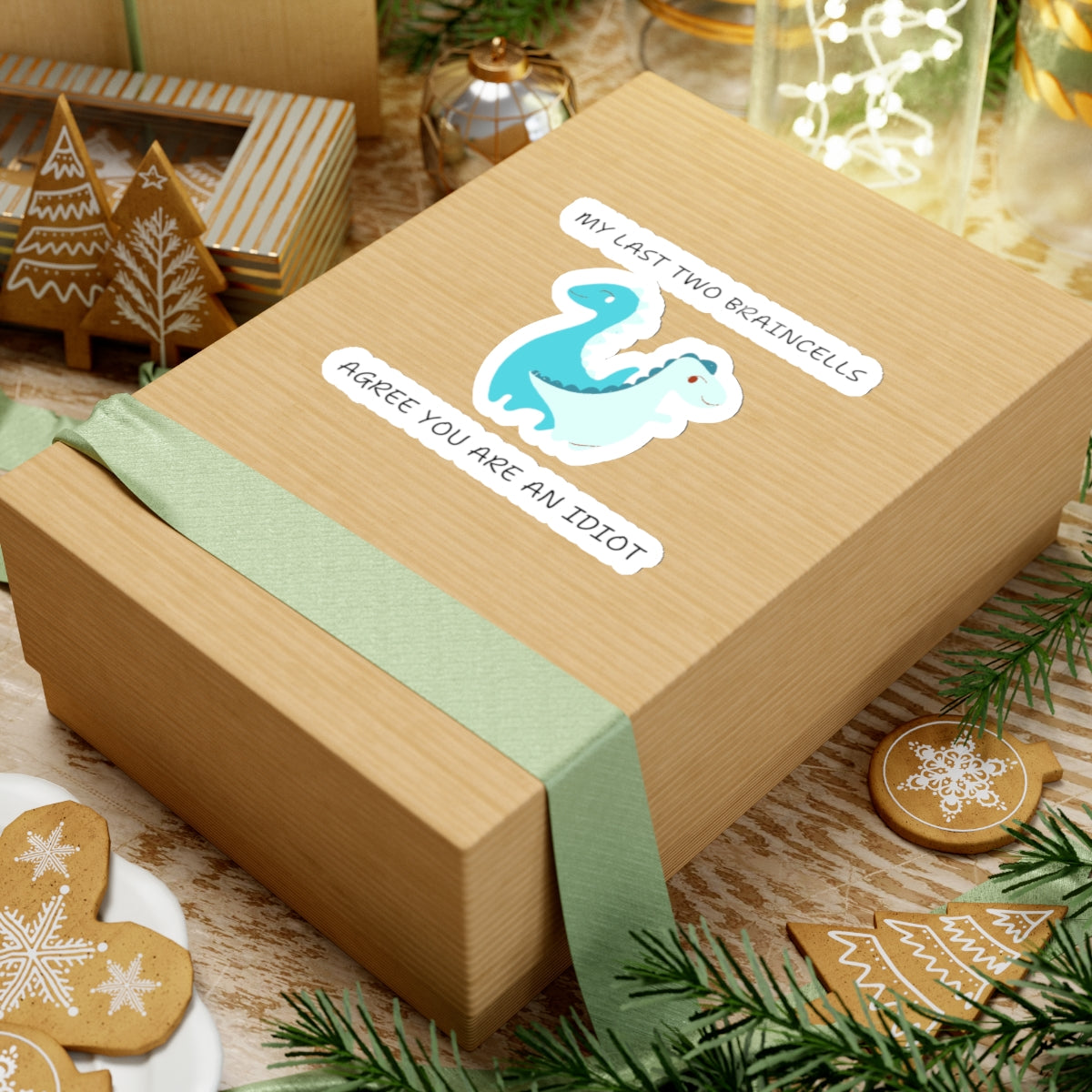 Brown gift box wrapped with green ribbon displaying cute dinosaur meme stickers from Printify on top