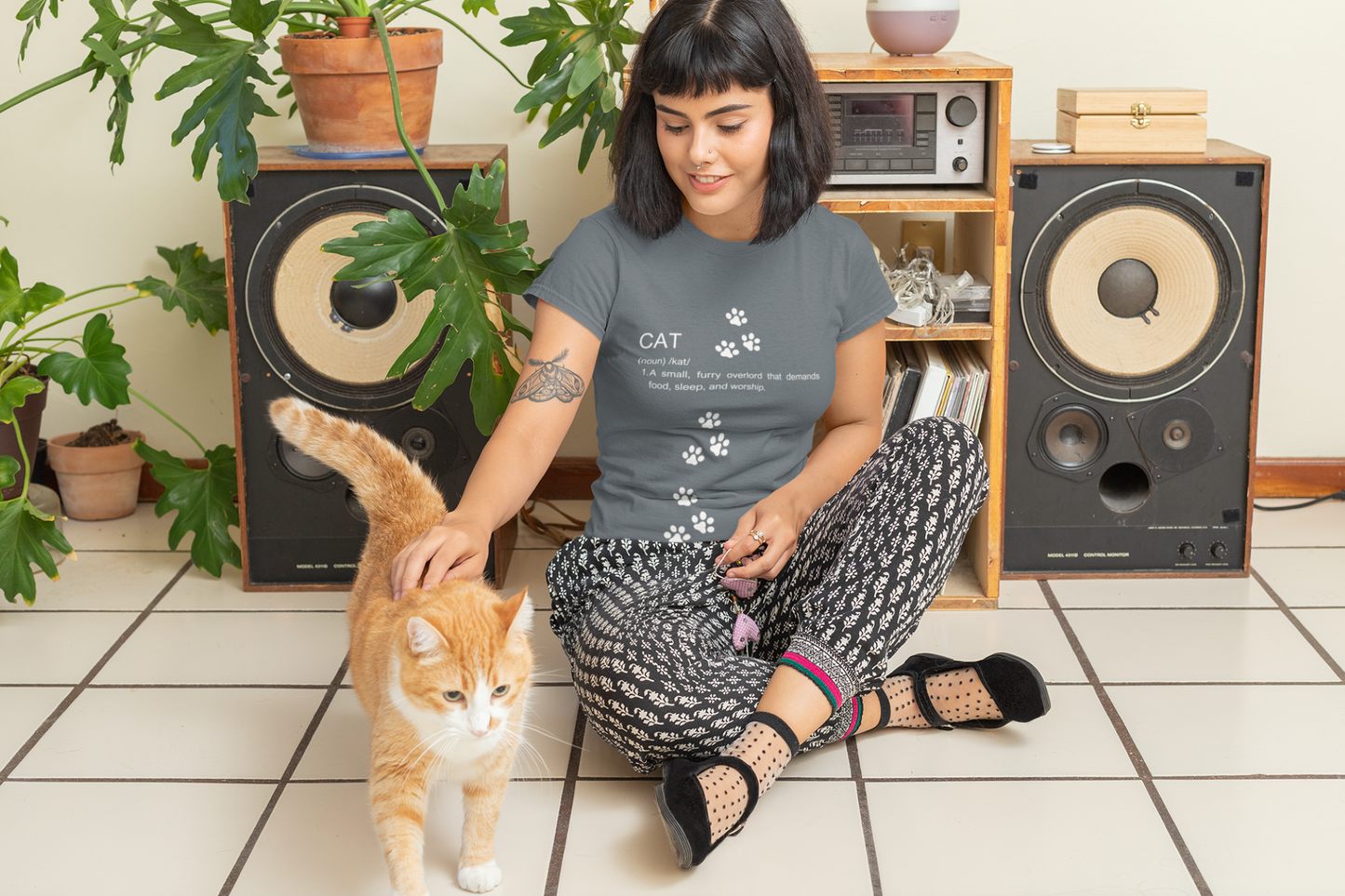 Funny cat definition t-shirt in gray worn by a woman petting an orange cat in a cozy living room