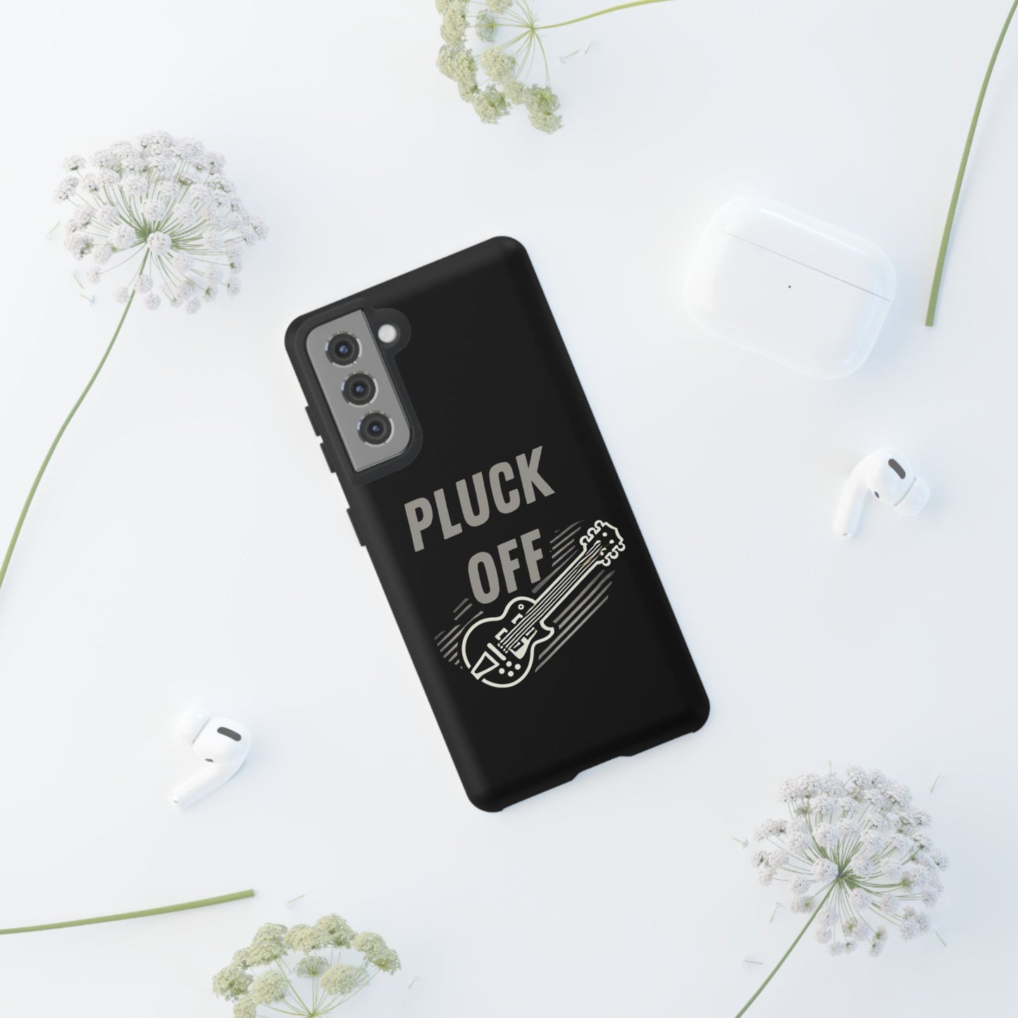 The Funny Pun Pluck Off Tough Phone Case, featuring a black dual-layer design with a guitar drawing and "PLUCK OFF" text, rests on a white surface surrounded by white flowers, wireless earbuds, and a charging case.