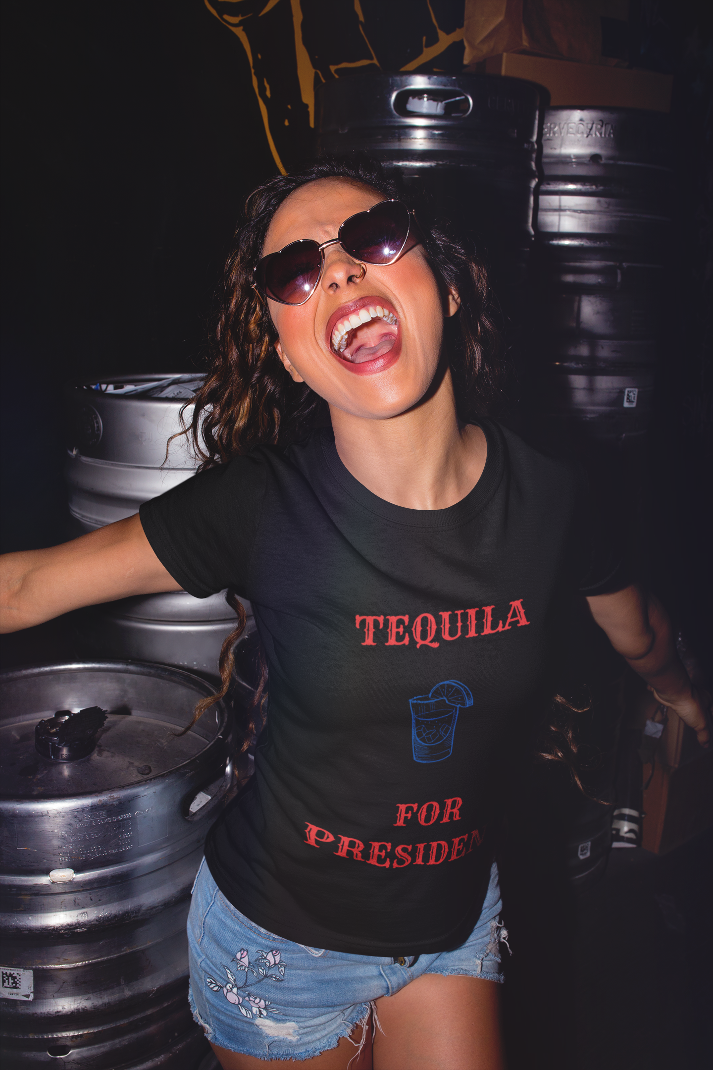 Smiling woman wearing Printify black tee with tequila for president political humor  t-shirt design in bar with beer kegs