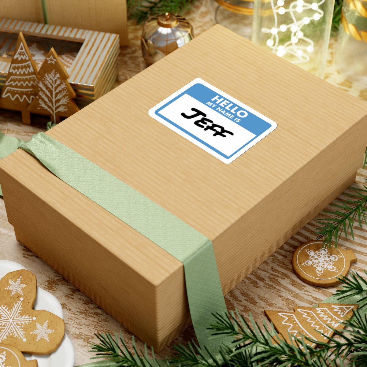 Gift box with a my name is Jeff sticker on top surrounded by holiday decorations and gingerbread cookies