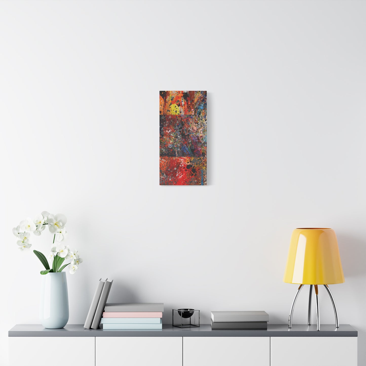 Red and orange abstract art canvas print hanging on wall over modern console with books and yellow lamp