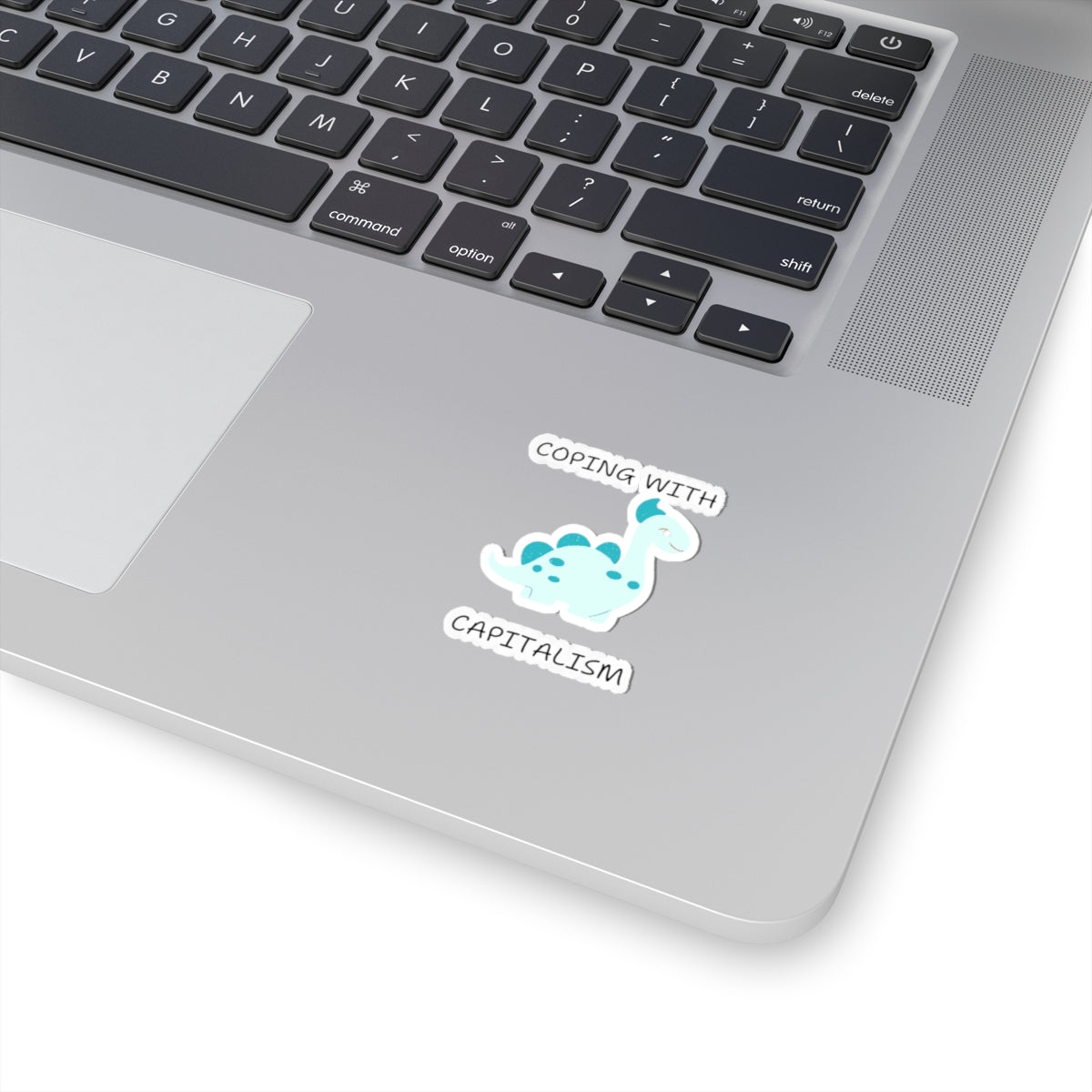 Unique sarcastic cute dinosaur sticker with blue spots on a silver laptop near keyboard