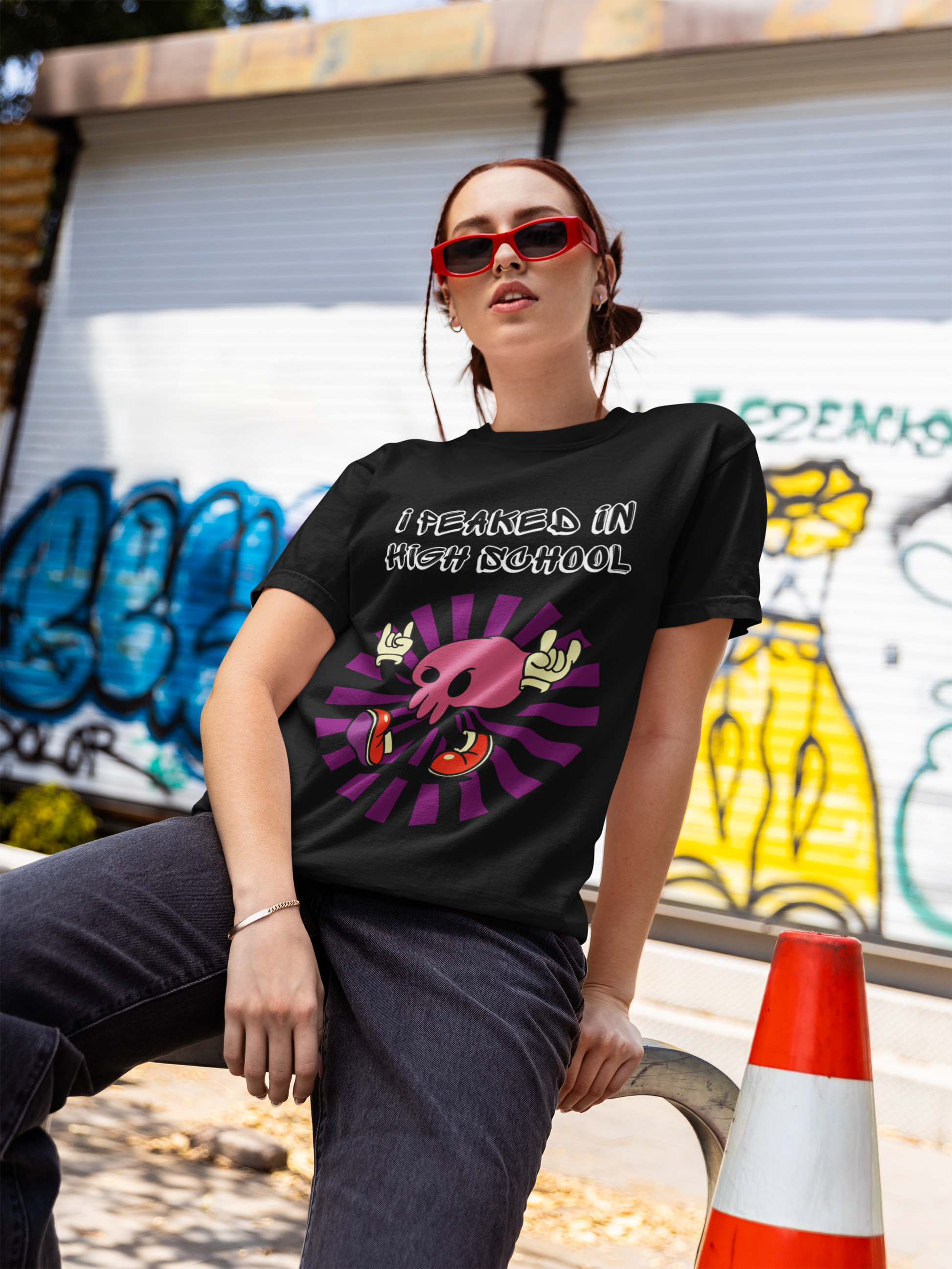 Printify black T Shirt model wearing I Peaked in High School funny t-shirt with skull graphic outdoors